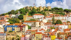 Un paysage urbain historique, avec un château imposant perché sur une colline, des bâtiments aux couleurs vives et un ciel dégagé.