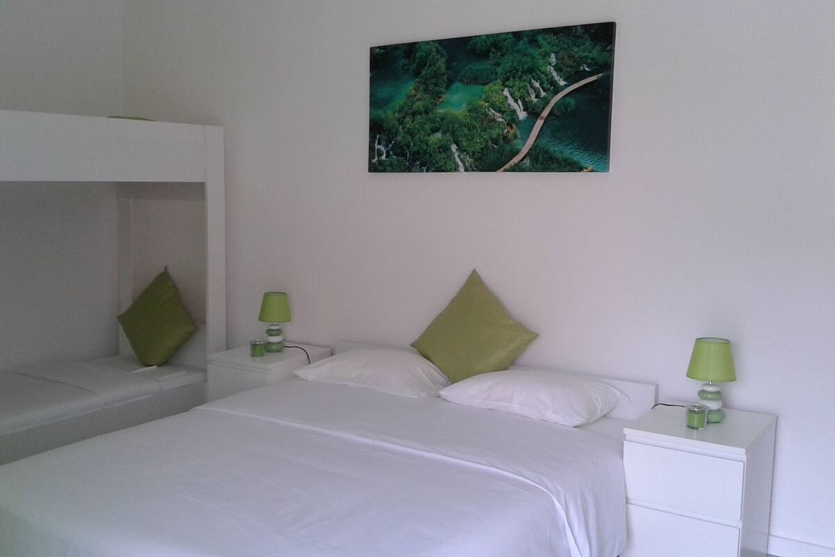 Une chambre avec deux lits simples, un lit superposé et une table de chevet avec une lampe.