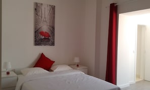 Una habitación de hotel con una cama, una mesita de noche, una lámpara, una cortina roja y un cuadro de la Torre Eiffel.