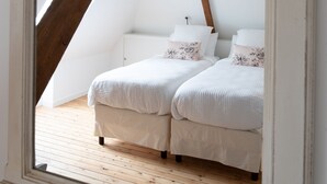 A bedroom with a sloped ceiling, wooden beams, two beds with floral bedding, and a large mirror reflecting the room.