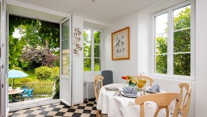 A dining area with a table set for four, a chair, a radiator, and a window with a view of greenery.