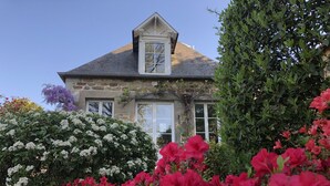 A stone house with a gabled roof, multiple windows, and a prominent chimney.