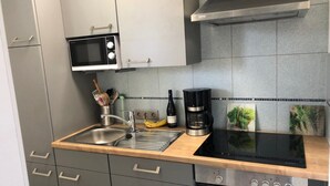 A modern kitchen with grey cabinets, a stainless steel sink, a microwave, a coffee maker, and a built-in oven. - Apartment am Kurpark - beautiful, quiet and right in the middle -  (St. Andreasberg)