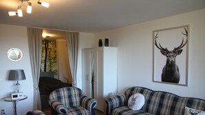 A living room with two plaid sofas, a round coffee table, a lamp, and a deer painting on the wall. - Apartment am Kurpark - beautiful, quiet and right in the middle -  (St. Andreasberg)