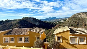 A yellow building with a tiled roof, surrounded by hills and a clear sky. - Magnificent quiet apartment close to everything with swimming pool. (Benitachell)