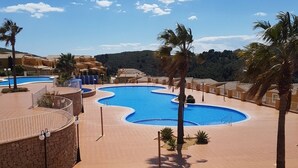 A resort pool area with multiple swimming pools, palm trees, and a mountainous backdrop. - Magnificent quiet apartment close to everything with swimming pool. (Benitachell)