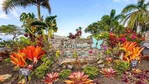 Eine Steinmauer mit der Beschilderung 'Kapalua Bay Villas', umgeben von tropischen Pflanzen und Blumen.