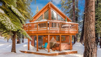 Une cabane dotée d’une terrasse en bois, de grandes fenêtres et d’un bain à remous.