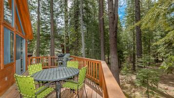 Une terrasse en bois avec une table ronde et des chaises, entourée de grands arbres.