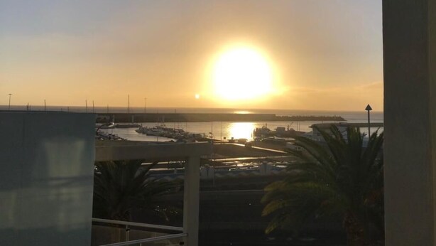 A sunset view from a balcony overlooking a marina with boats and a distant shoreline. - RESIDENTIAL JANDIA MARINA 111 (Morro Jable)