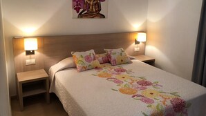 A hotel room with a bed, two bedside lamps, a nightstand, and a wall-mounted artwork of a seated figure. - RESIDENTIAL JANDIA MARINA 111 (Morro Jable)