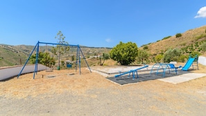 Un parque infantil con columpios, tobogán y equipo de ejercicio en un entorno rural.