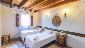 A hotel room with two single beds, wooden headboards, a small wooden table, a nightstand, a wall-mounted lamp, and a woven wall decoration. - El Zorro Almáchar by Ruralidays (Málaga)