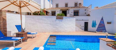 A swimming pool with blue lounge chairs and a brick wall.
