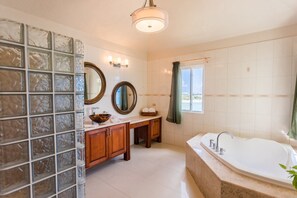 Un baño con una bañera grande, un tocador con espejo y una pared de bloques de vidrio.