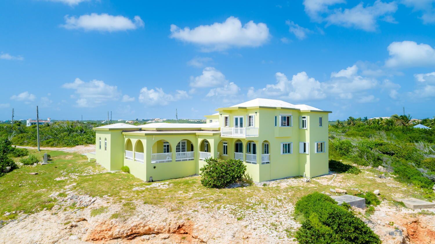 A two-story building with a light green exterior and a white roof, featuring multiple balconies and arched windows.