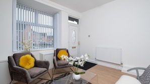 A modern living room with two grey armchairs, a white door, and a window with blinds. - Bachuss Lodge (Birmingham)