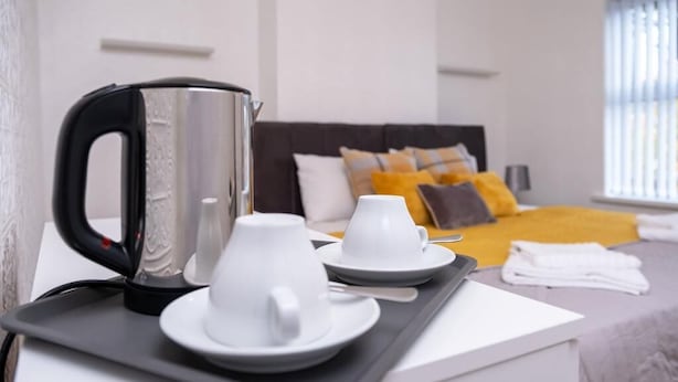 A hotel room with a bed, pillows, a tray with a kettle, cups, and a spoon. - Bachuss Lodge (Birmingham)