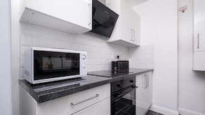 A modern kitchen with white cabinetry, a microwave, and a built-in oven. - Bachuss Lodge (Birmingham)