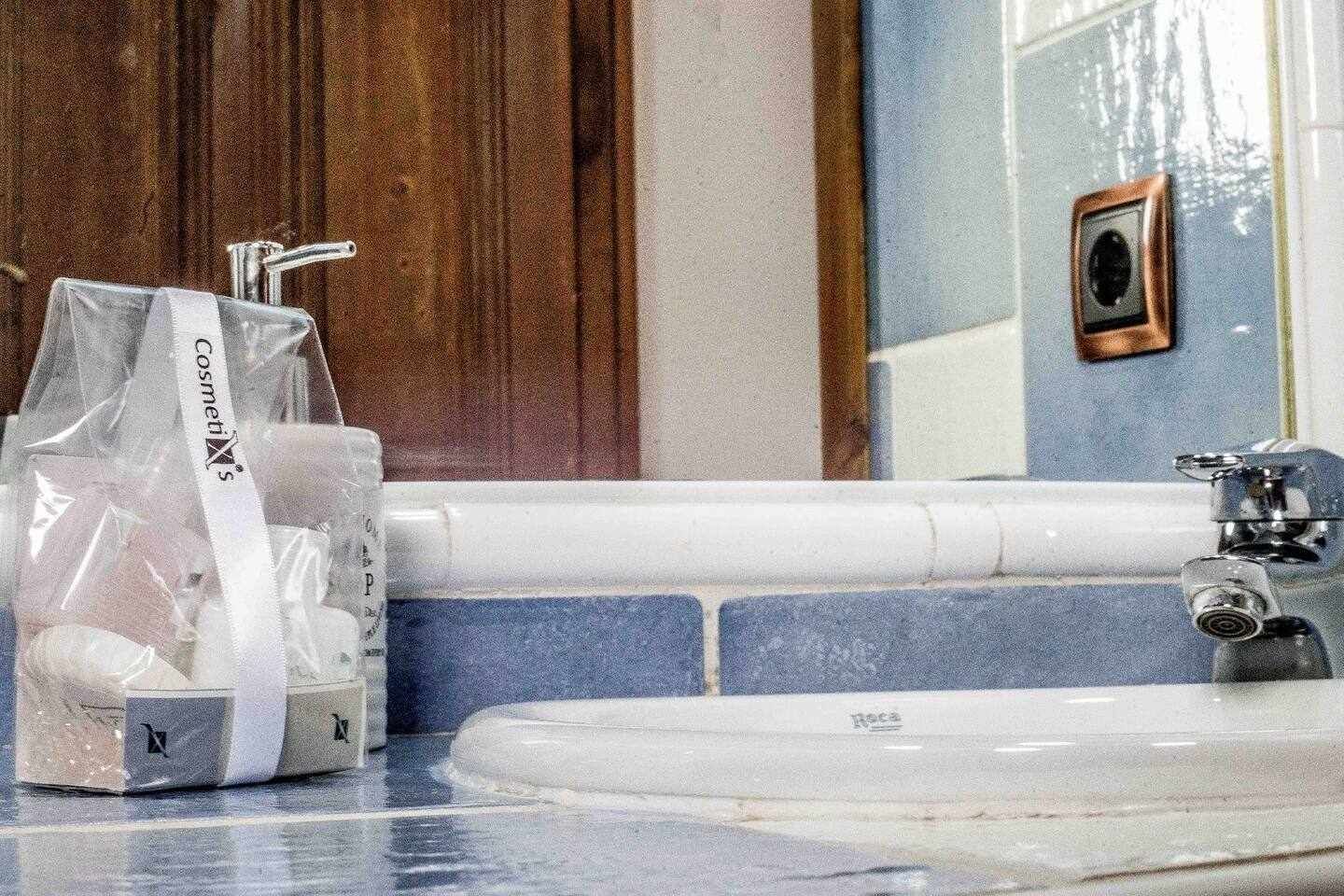 Une salle de bain avec un lavabo blanc, des carreaux bleus, une porte en bois et un sac étiqueté « Cosmetix ».
