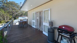 Een balkon met een houten terras, een tafel met stoelen, een barbecue en een terrasverwarmer.
