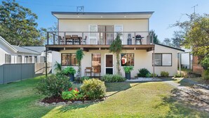 Een tweelaags huis met een balkon, een voordeur en een kleine tuin met verschillende planten en bloemen.
