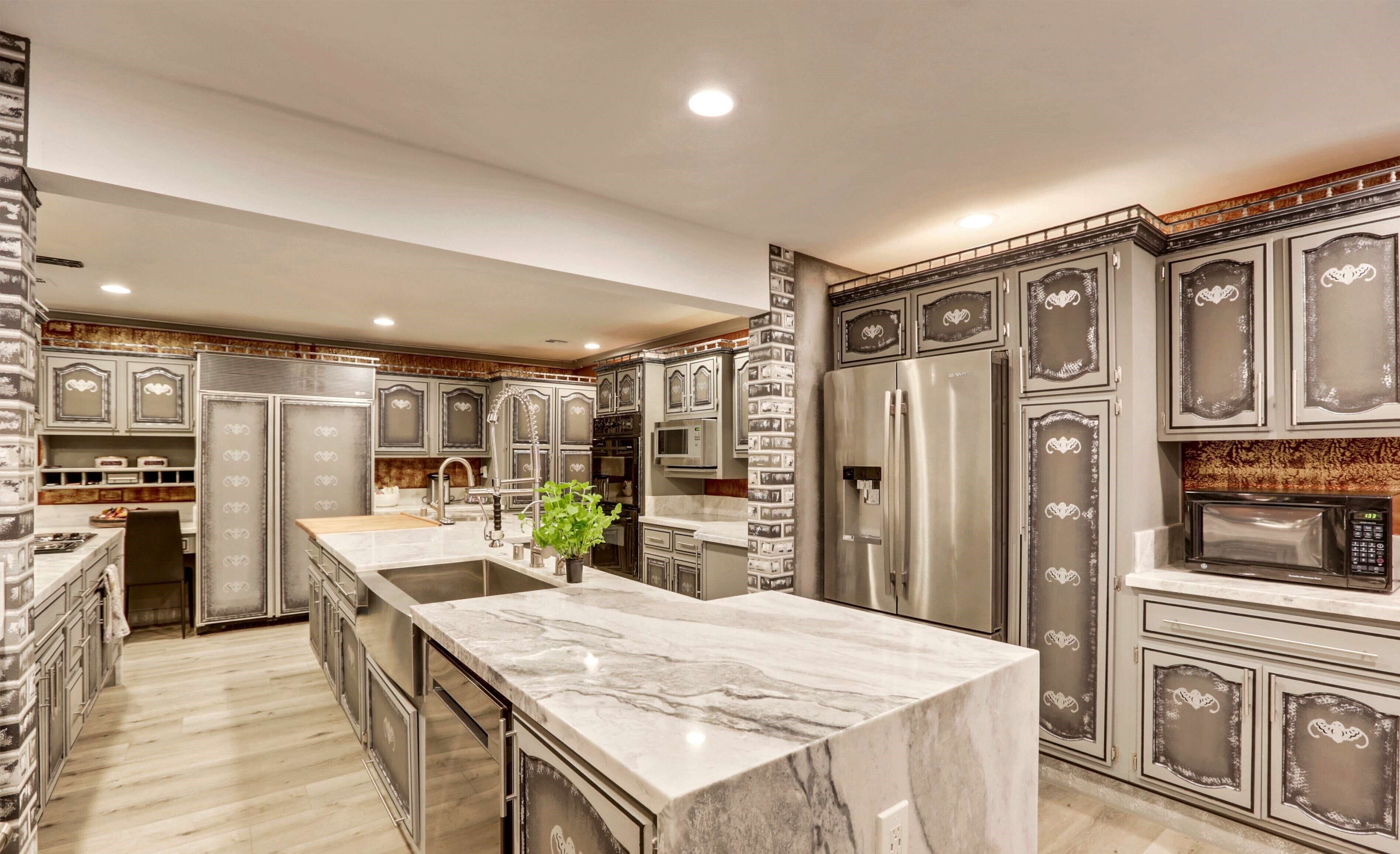 A modern kitchen with marble countertops, stainless steel appliances, and decorative cabinetry.