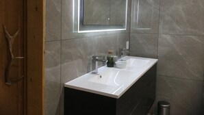 A modern bathroom with a white sink, a mirror, and a glass bottle of soap.