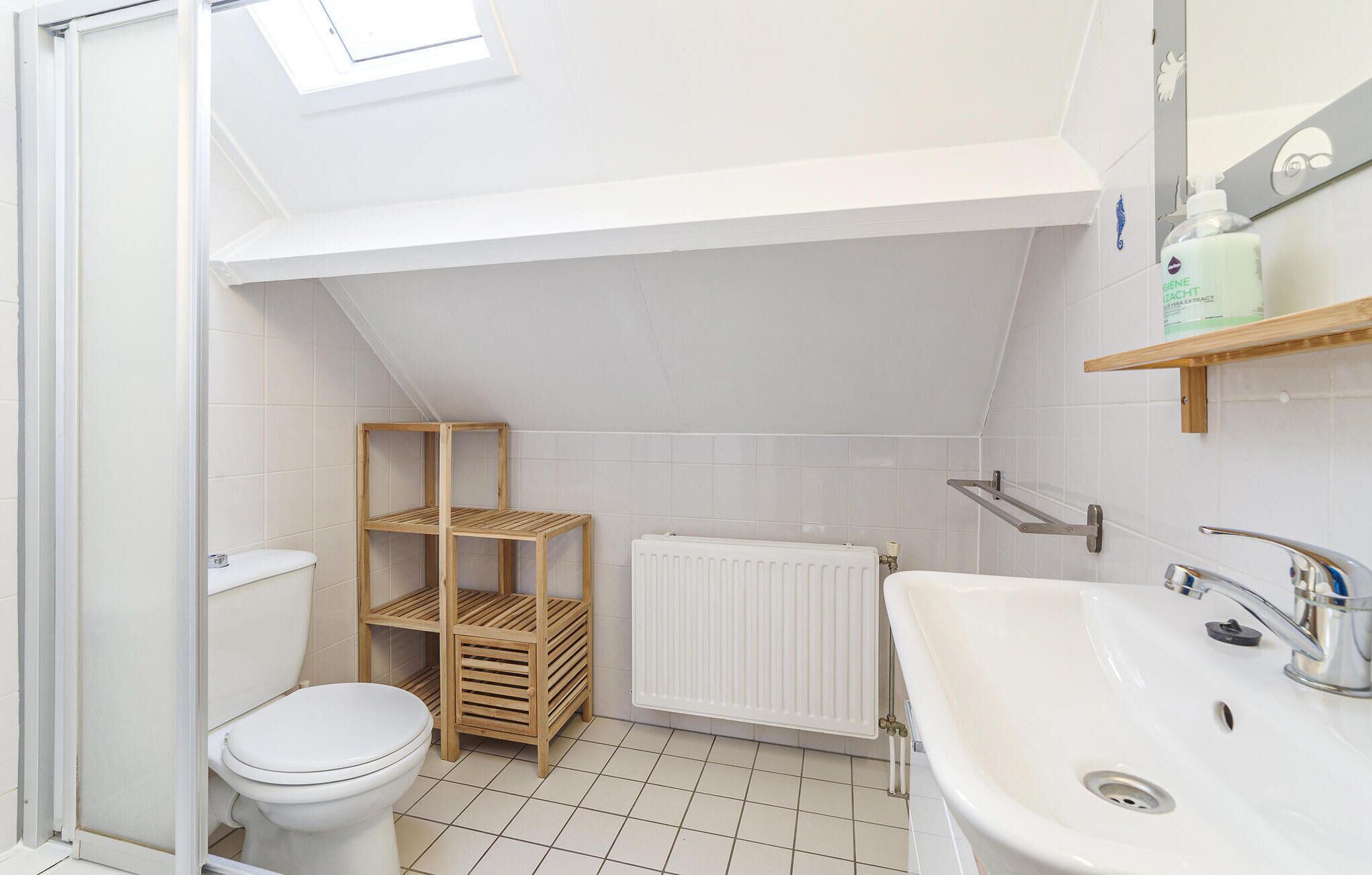 Ein kleines Badezimmer mit Toilette, einer Holzregaleinheit, einem Heizkörper und einem Waschbecken mit Spiegel darüber.