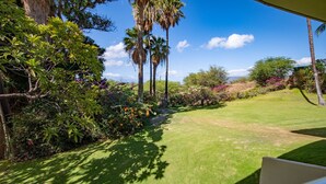 Un jardín bien cuidado con diversas plantas y árboles, cielo despejado y un césped frondoso.