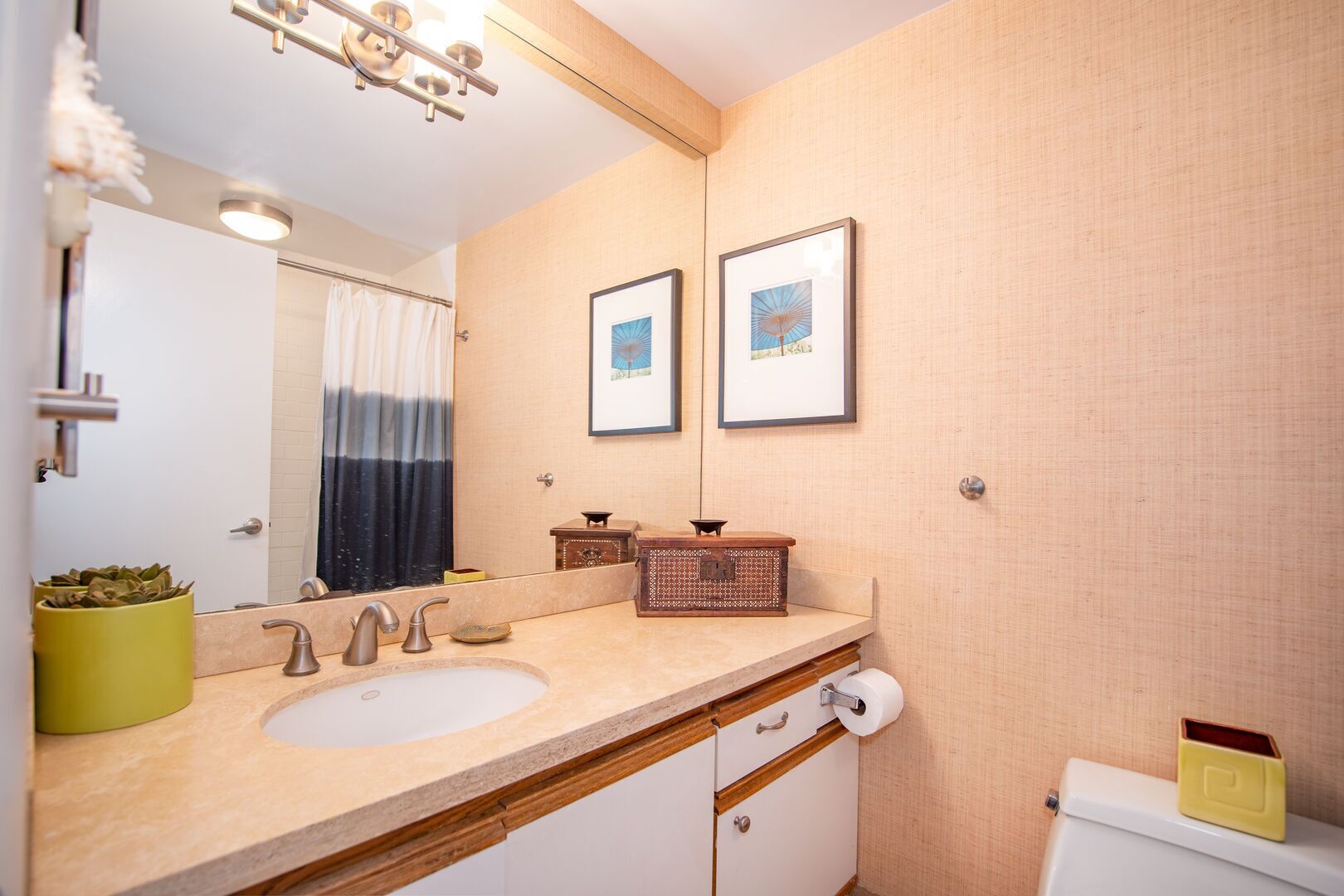 A bathroom with a sink, mirror, and toilet. There are framed pictures on the wall and a small plant on the counter.