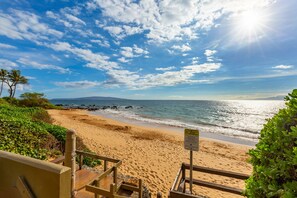 A beach with a wooden staircase leading down to the shore, a sign warning about the water, and a clear view of the ocean and sky. - Prime Location Near South Maui's Top Beach (Kihei)