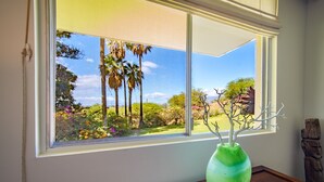 Una ventana con vista a un jardín, un jarrón verde con ramas y una mesa de madera.