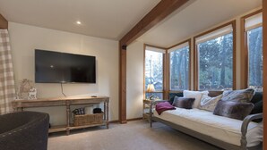 Una habitación acogedora con una cama, un televisor y ventanas amplias que dan a unas arboledas.