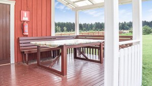 Een overdekt buitengebied met houten banken en een picknicktafel, een brandblusser bevestigd aan de muur, en uitzicht op een bebost landschap.