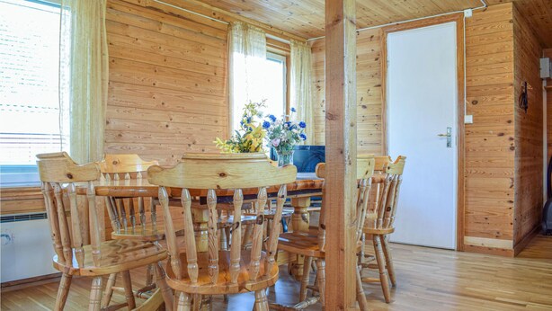 Een houten interieur met een ronde houten tafel, omringd door stoelen, een deur en een raam met gordijnen.