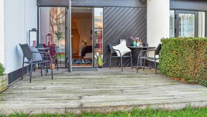Et udendørs opholdsområde med træterrasse, to borde og fire stole.