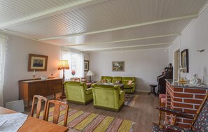 Un saló confortable amb zona de menjador, amb cadires tapissades de verd, taula de dinar de fusta i una paret d'accent de maó.