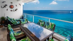 A balcony with wicker furniture, a glass table, and a view of the ocean. - Amazing Ocean Views (Cozumel)