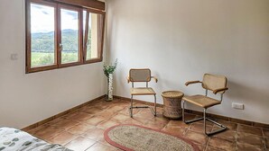 Een kamer met een groot raam, twee rieten stoelen, een klein tafeltje en een geweven vloerkleed.