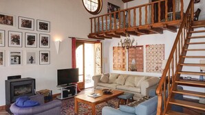 Een woonkamer met een bank, fauteuils, een televisie, een open haard en een trap.