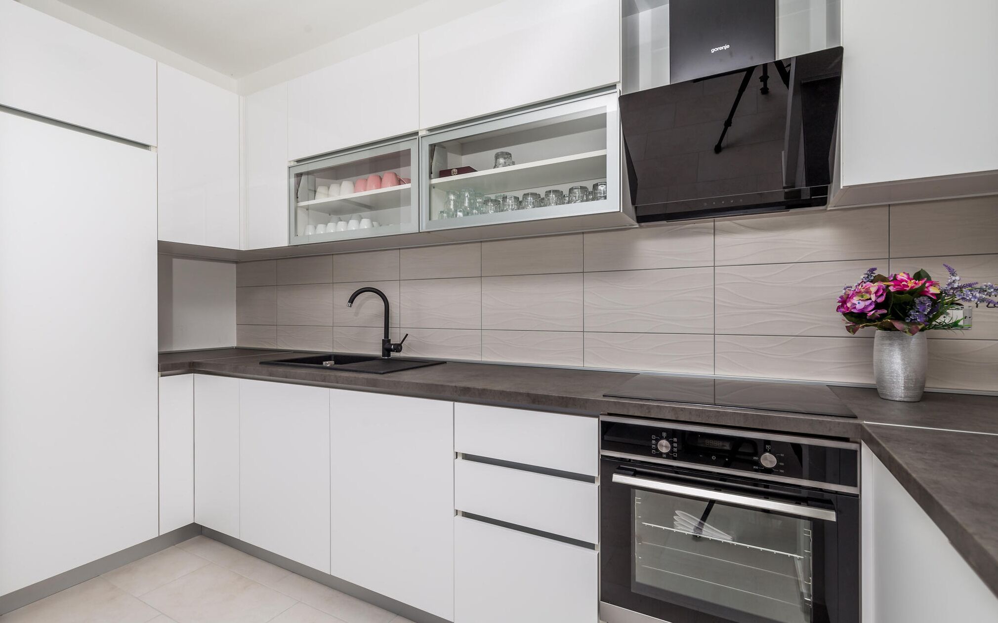 Une cuisine moderne avec des meubles blancs, un évier noir et un four en acier inoxydable.