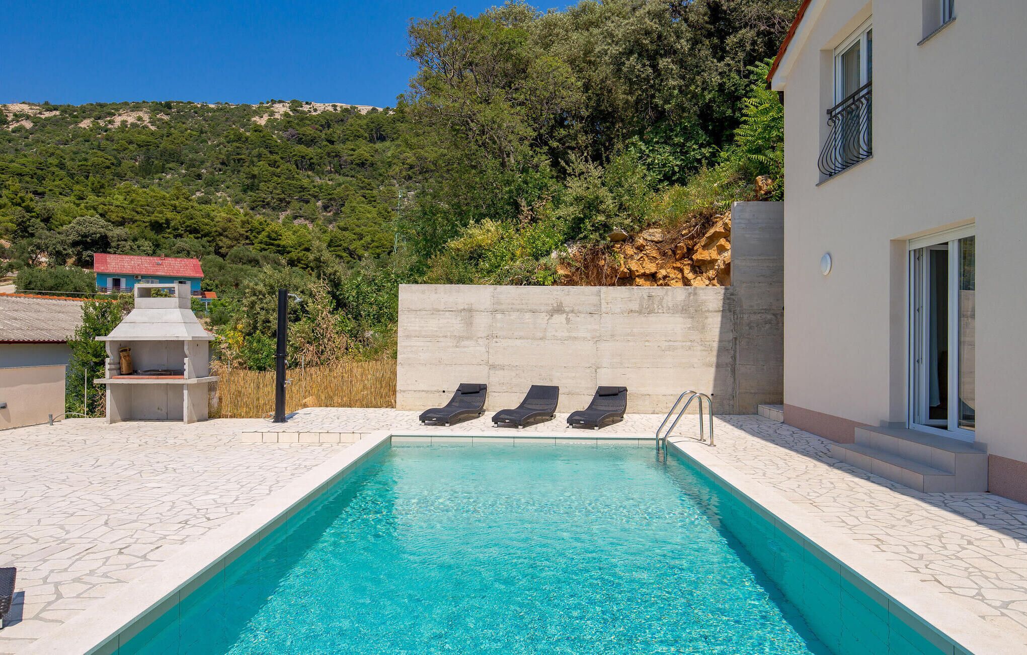 Una piscina con sillas de descanso, zona de barbacoa y vistas a una colina.