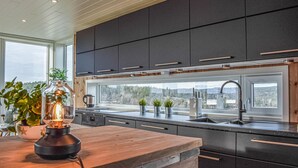 A modern kitchen with dark cabinets, a wooden countertop, and a large window overlooking a forested area.