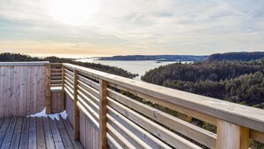 A wooden deck with a railing overlooking a body of water and forested hills.