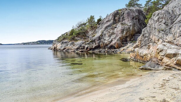 A coastal beach with rocky cliffs and clear water.