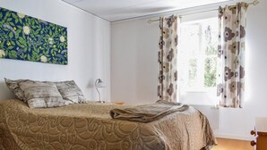 Un dormitorio con cama, almohadas, una lámpara y un ventanal con cortinas.
