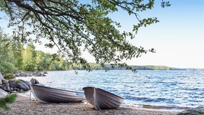 Dos barcos amarrados a una orilla rocosa con un bosque y un lago al fondo.