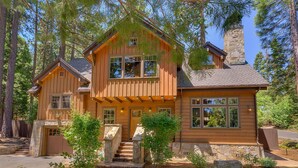 A two-story log cabin with a stone chimney, a front porch, and a stone staircase leading to the entrance. - Holly Hideaway - TLUXP (Tahoe City)
