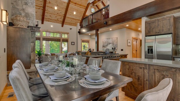 A spacious dining area with a long table set for six, a kitchen with modern appliances, and a loft with wooden beams. - Holly Hideaway - TLUXP (Tahoe City)